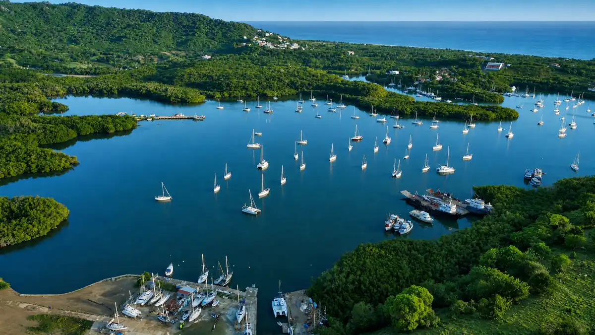Wide aerial view of Luperón’s mooring field showing many anchored sailboats in protected waters.